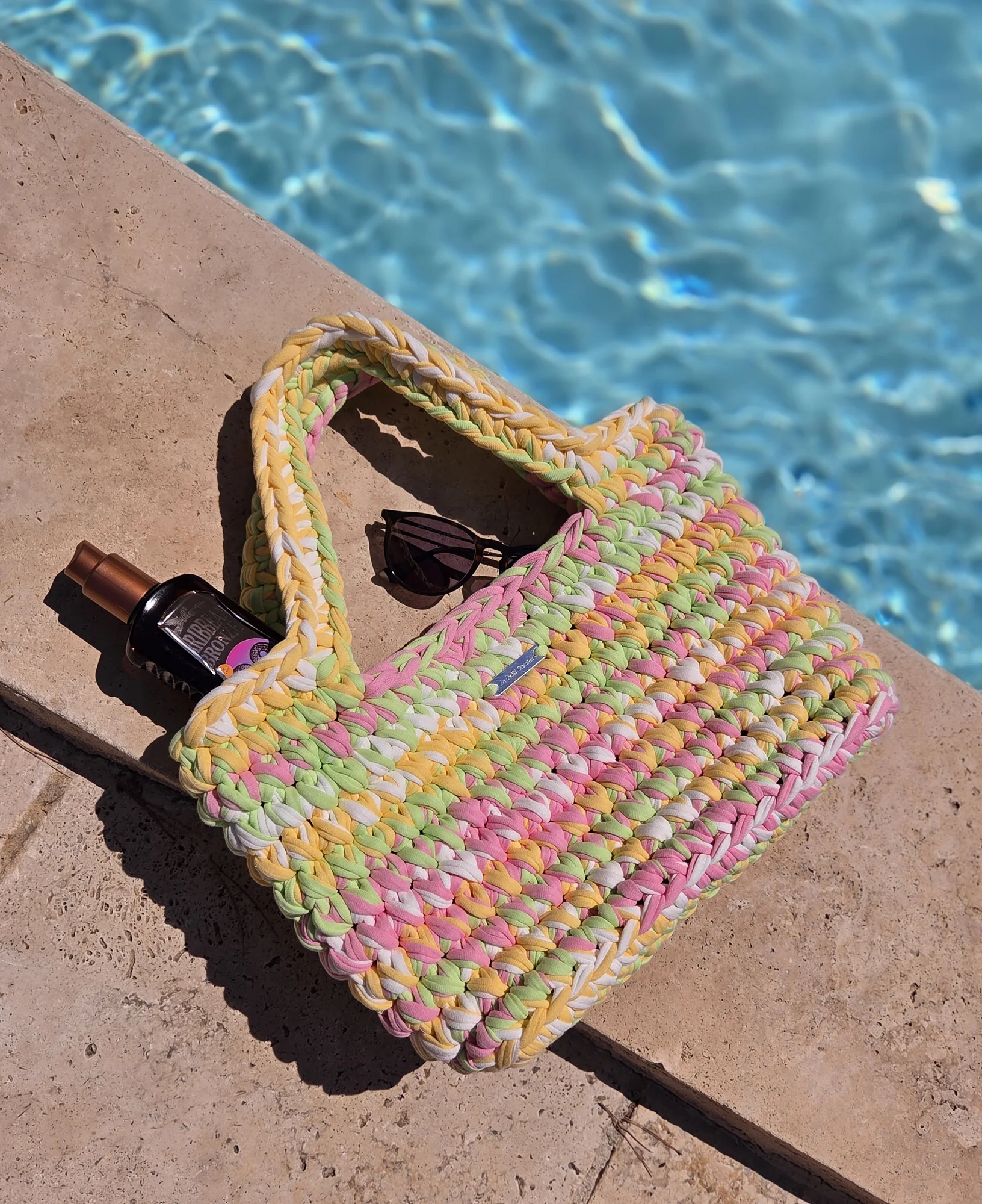 Cabas Siena au crochet, pièce unique Macaron : jaune clair, vert pâle, rose pâle et blanc, posé au bord d'une piscine